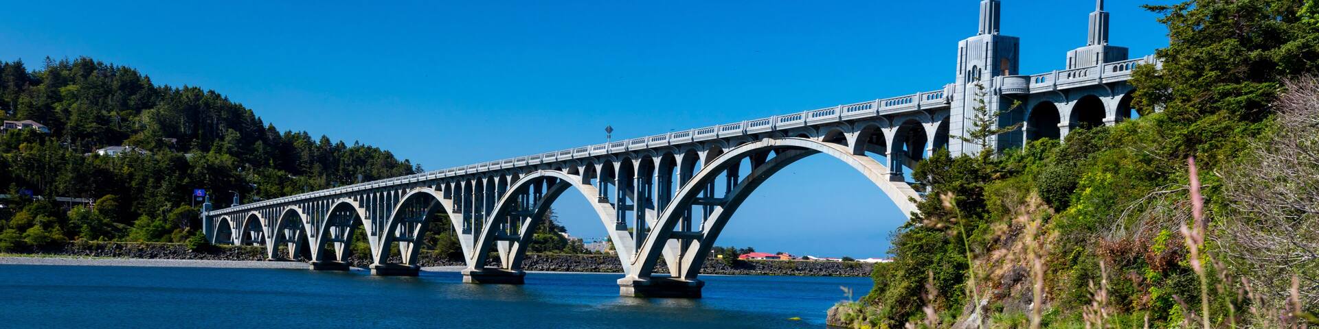 A bridge over a calm river, surrounded by lush greenery and vibrant flowers.