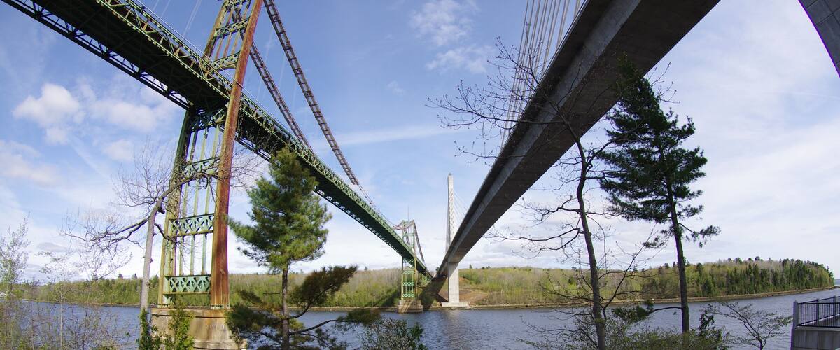 A suspension bridge over a calm river with trees and a clear sky.