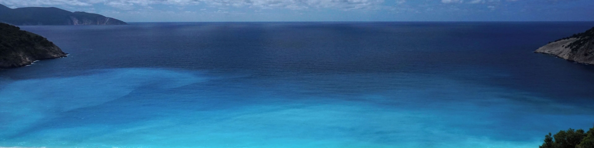 The majestic Myrtos beach (Kefalonia) as seen from the hairpin road: white pebbles, deep blue water, surrounded by white rocky cliffs and endless green hills #LifeAtExpedia #SeasideDiscoveries