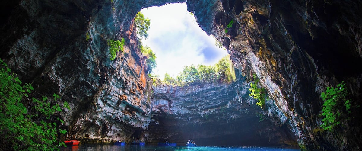 A cave opening with clear water and boats inside.