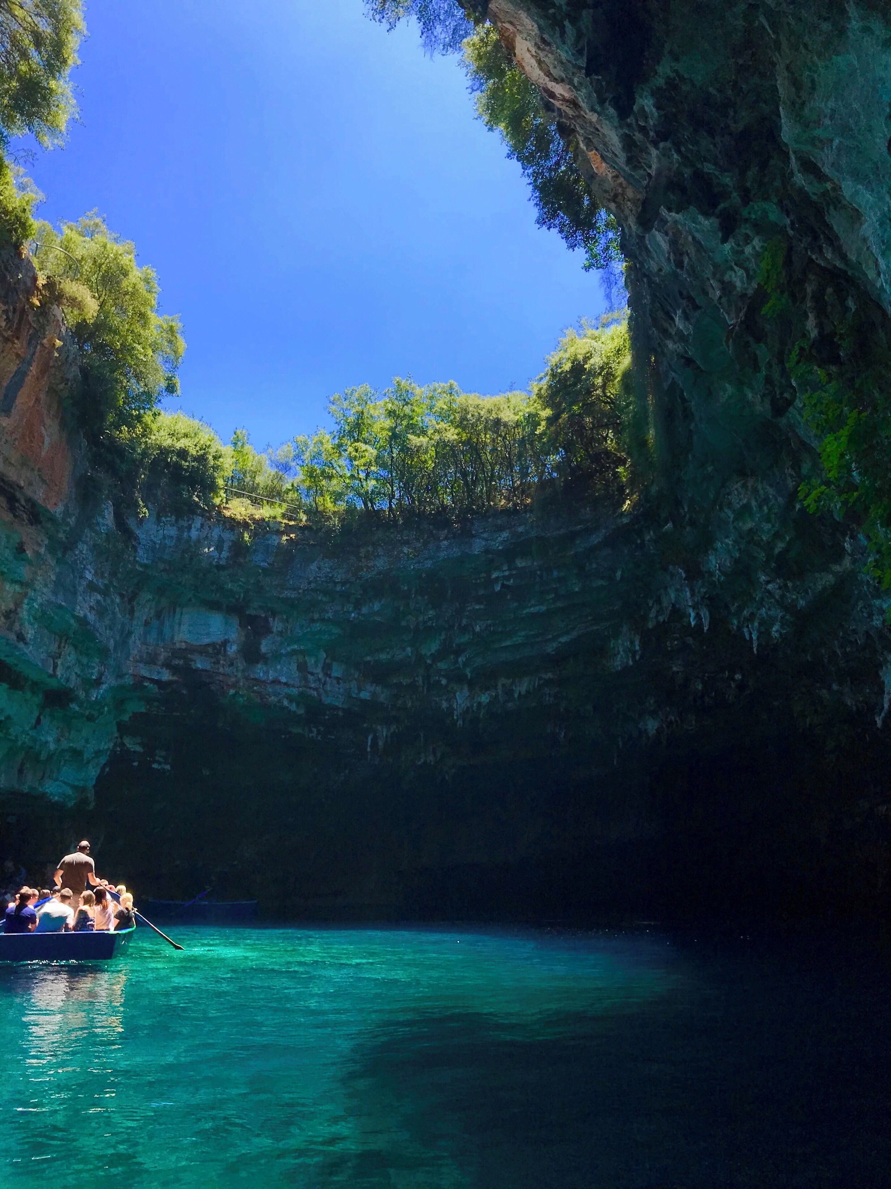 A boat in a clear blue water body surrounded by rocky cliffs and lush greenery.