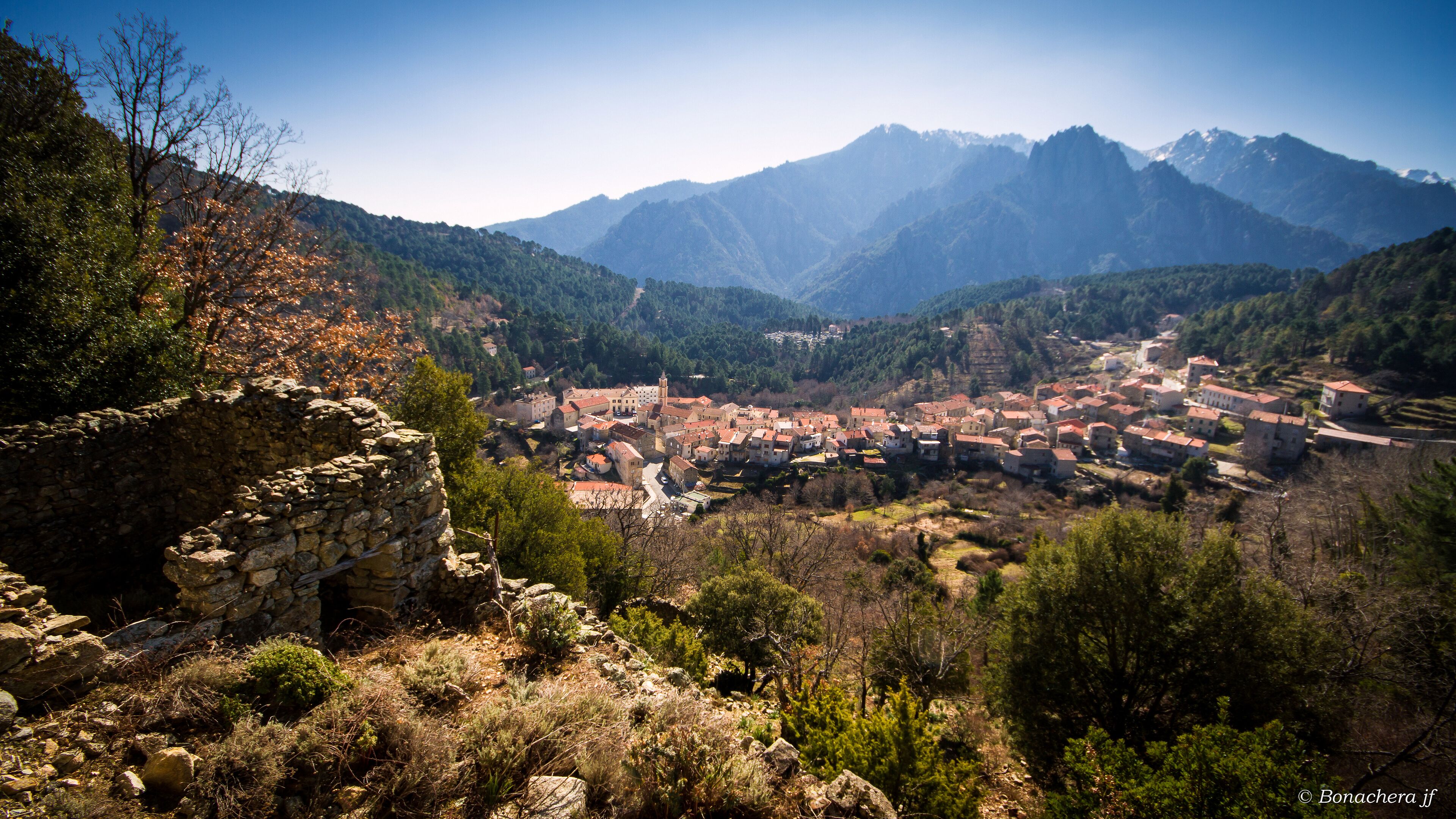 A mountainous landscape with a village nestled in the valley, surrounded by dense forests and rocky terrain.
