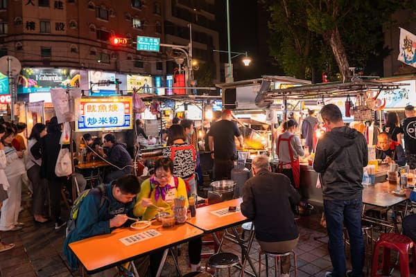 A bustling night market with food stalls and people dining.