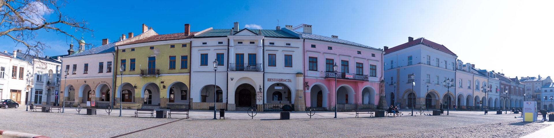 A cobblestone square with colorful buildings, benches, and a clear blue sky.