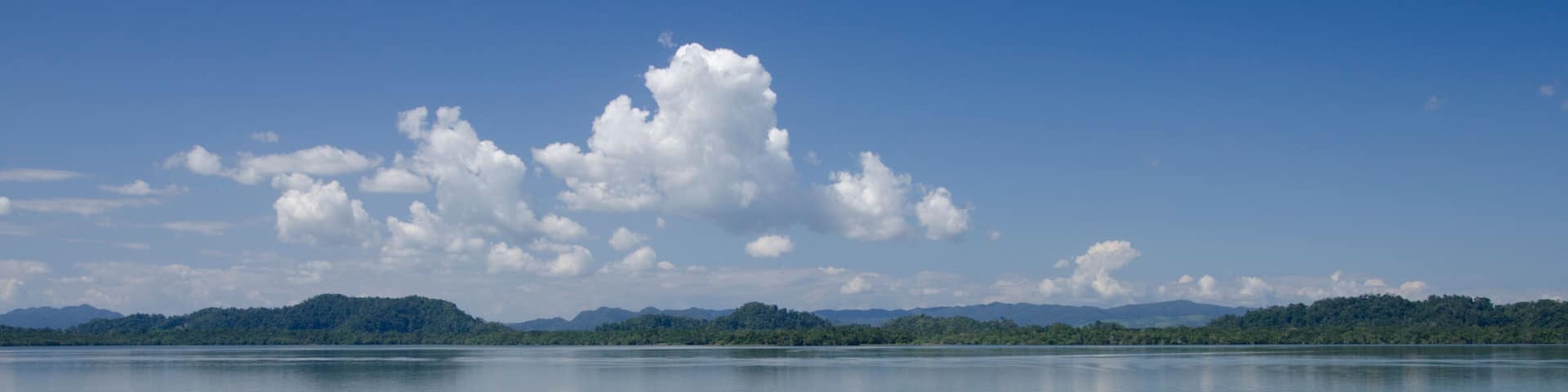 A calm lake with a clear sky and a large cloud.