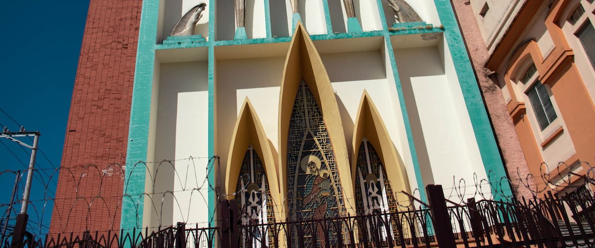 A church with a cross on top, a large statue in front, and a fence in the foreground.