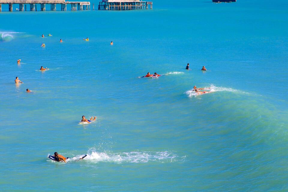 Una playa con gente nadando y practicando surf.