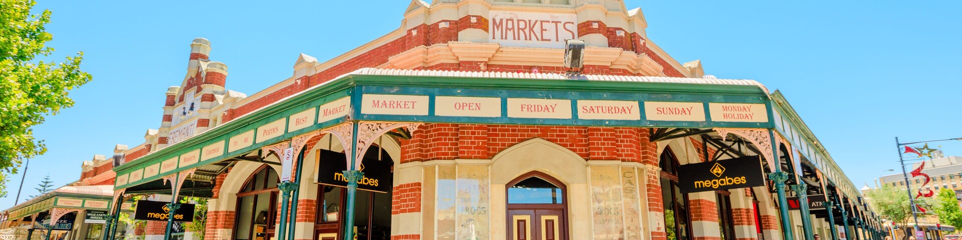 Un edificio de mercado con una fachada distintiva en rojo y crema, puertas en arco y señalización que indica los días de mercado.