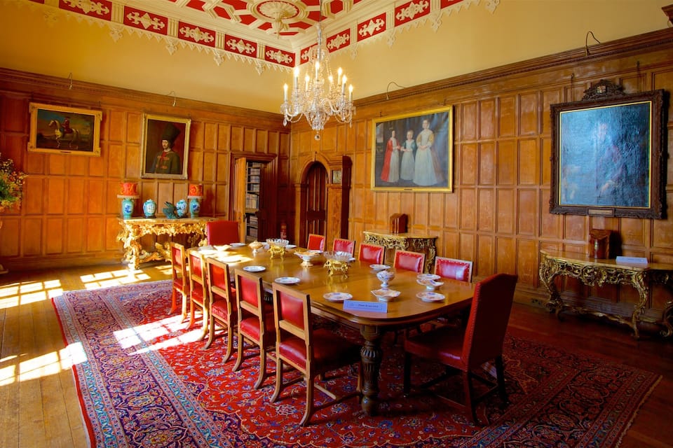 Een statige eetzaal met een lange houten tafel, rode fauteuils, gedetailleerd houtwerk en een kroonluchter.