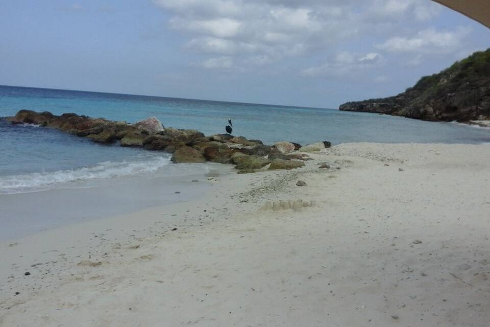 A beach with white sand, calm blue waters, and rocky outcrops.