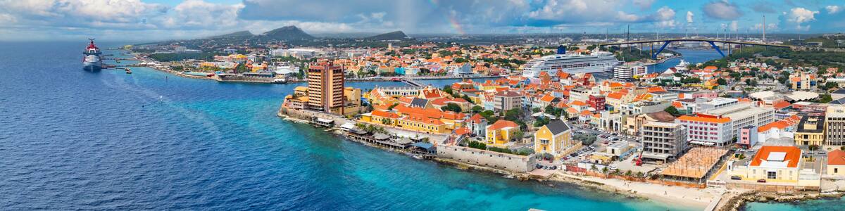 A coastal city with a prominent cruise ship docked, a rainbow, and a bridge in the distance.