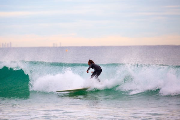 Um surfista deslizando numa onda, com um horizonte urbano ao fundo.