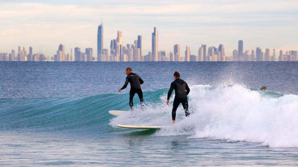 Two surfers on a wave with a city skyline in the background.