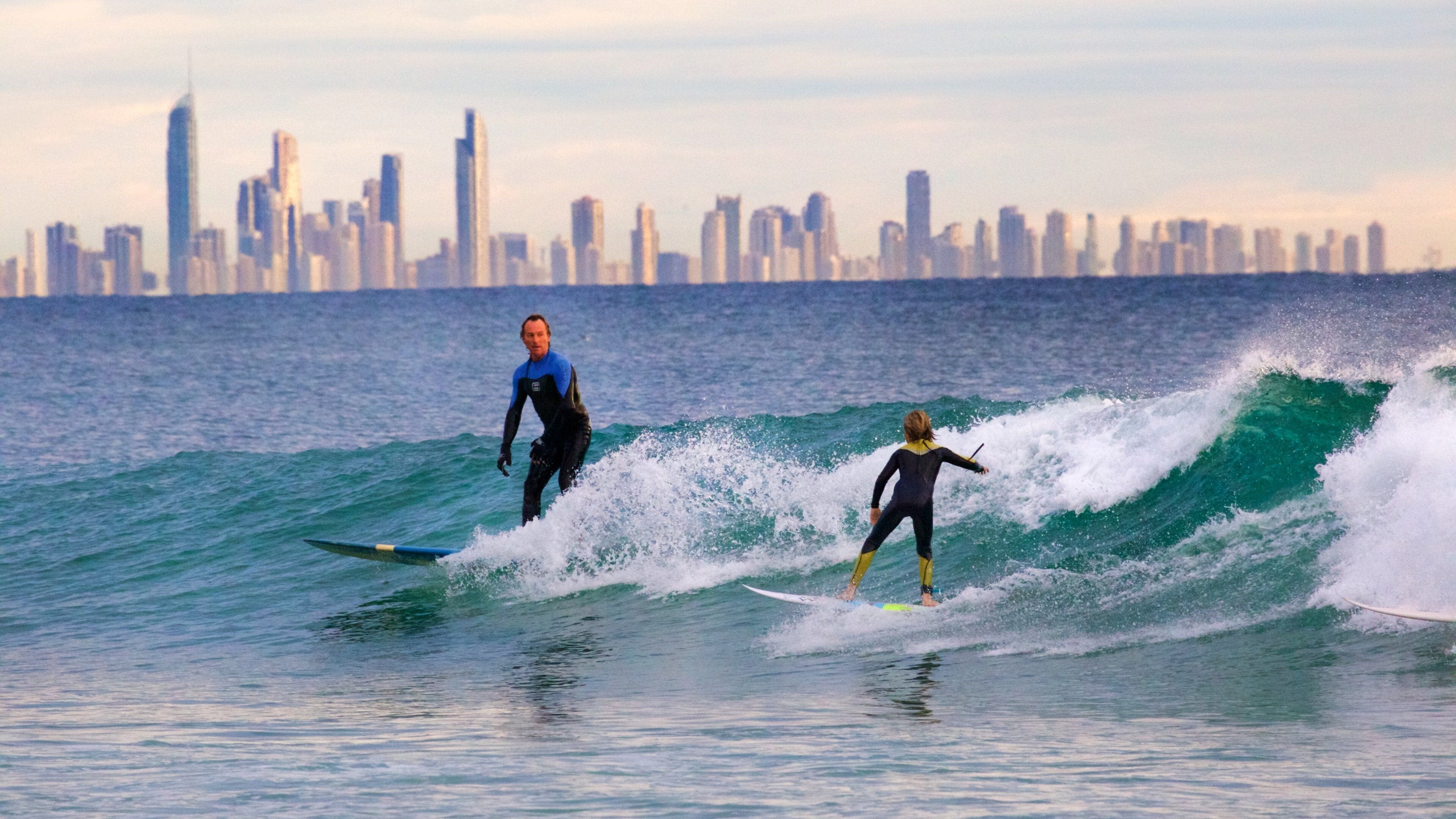 Deux surfeurs sur une vague, avec la silhouette d’une ville en arrière-plan.