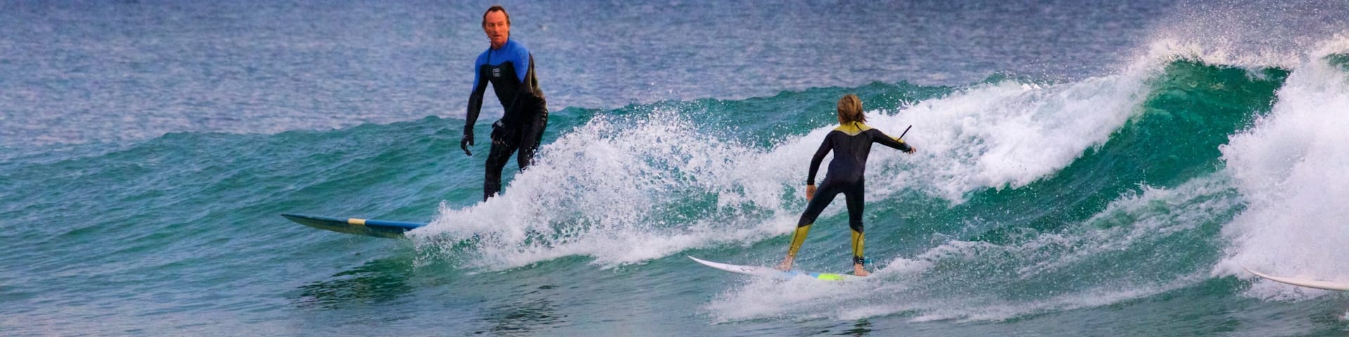 Two surfers on a wave with a city skyline in the background.