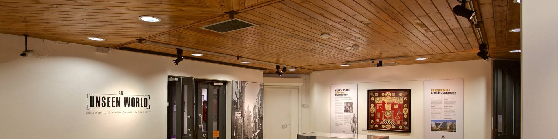 An art gallery with wooden floors and ceiling, displaying various artworks and informational posters.