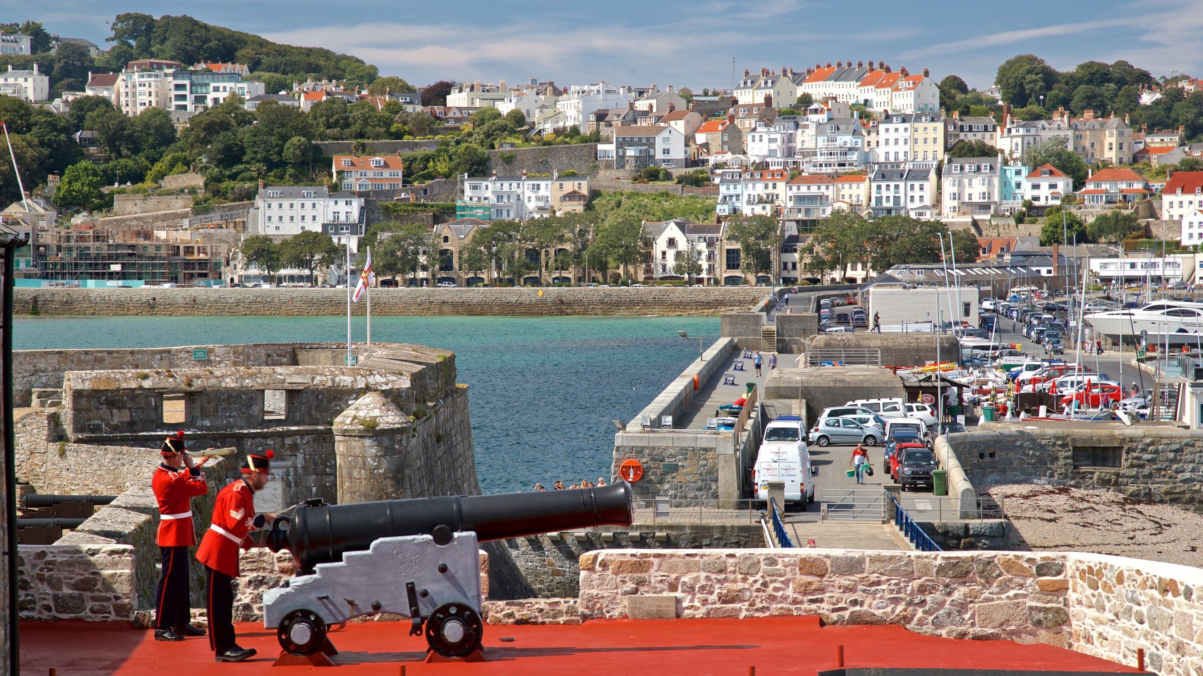 A coastal town with a historic cannon, stone walls, and a marina.