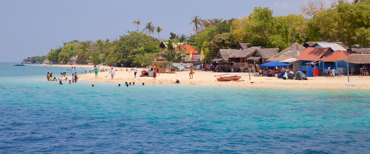 A beach with clear turquoise water, people swimming, and thatched-roof huts.