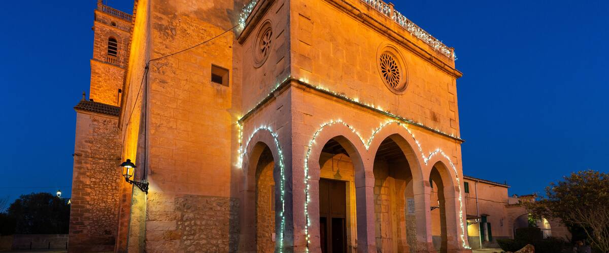 A historic building with illuminated arches and a clock tower at dusk.