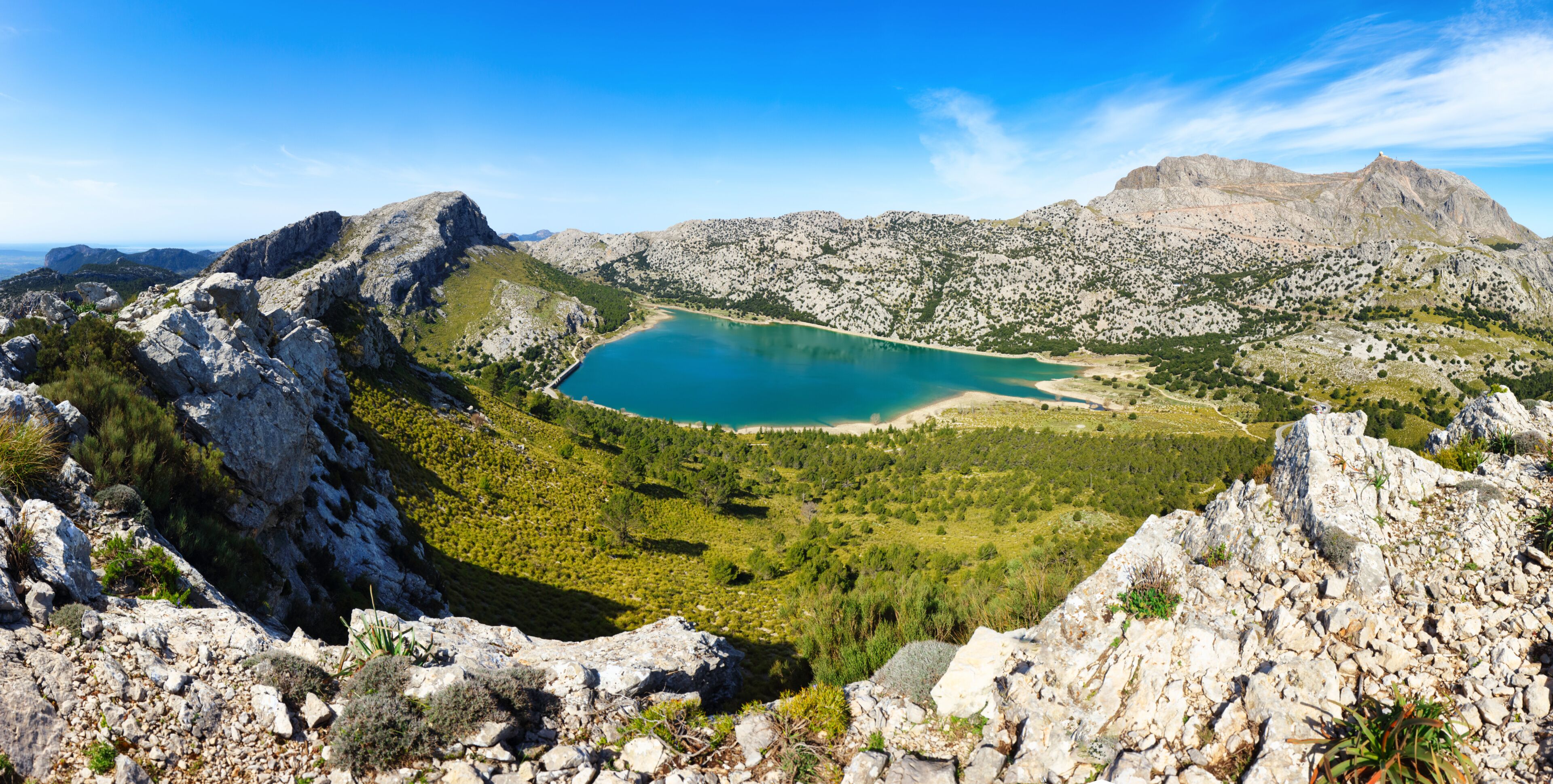 A mountainous landscape with a turquoise lake surrounded by rocky terrain and sparse vegetation.