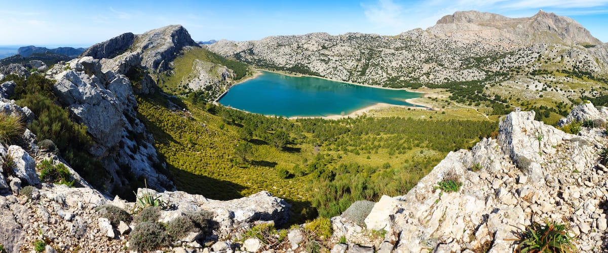 A mountainous landscape with a turquoise lake surrounded by rocky terrain and sparse vegetation.