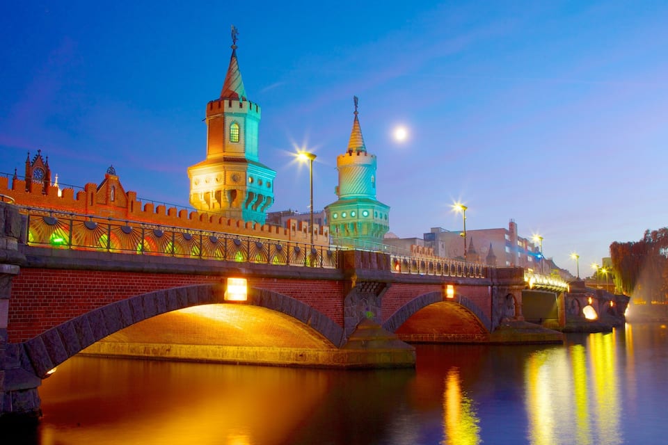 Een historische brug met verlichte torens en een rustige rivier die de lichten weerspiegelt.