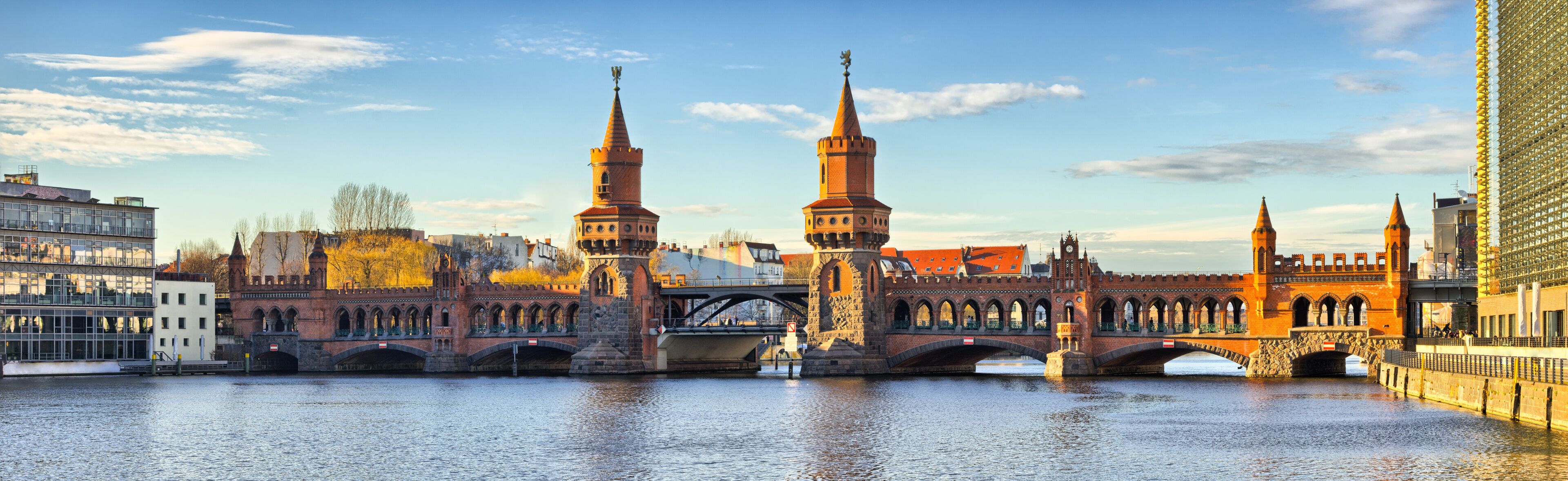 A historic bridge with two towers, a river, and modern buildings in the background.