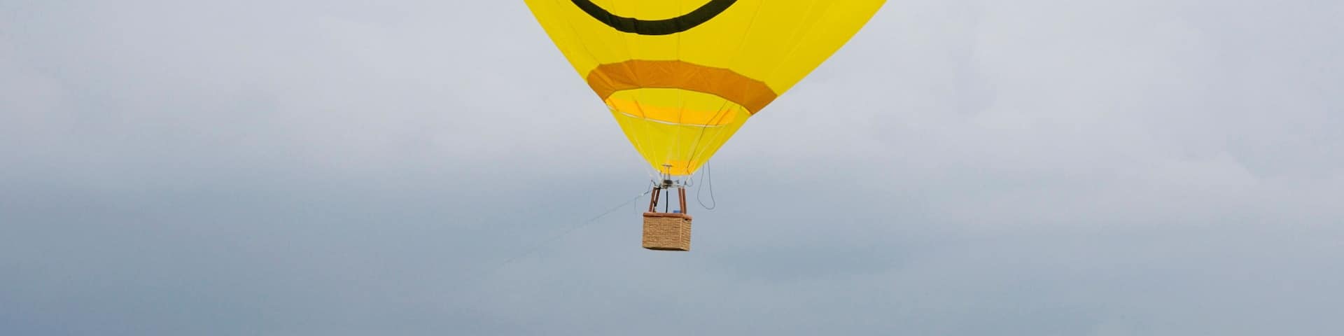 Yellow balloon with the smiley face symbol on it flying in the cloudy sky