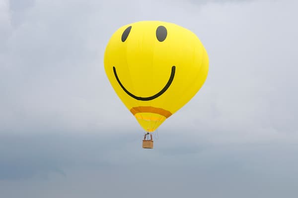 Yellow balloon with the smiley face symbol on it flying in the cloudy sky