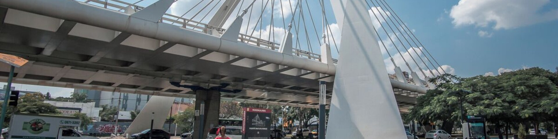 Un paso de peatones con una estructura de puente moderna, un cartel y una fila de bicicletas.