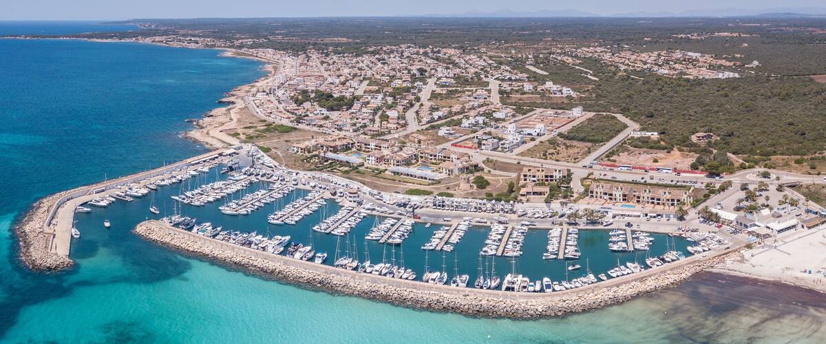 An aerial view of a coastal town with a marina, clear blue waters, and surrounding greenery.