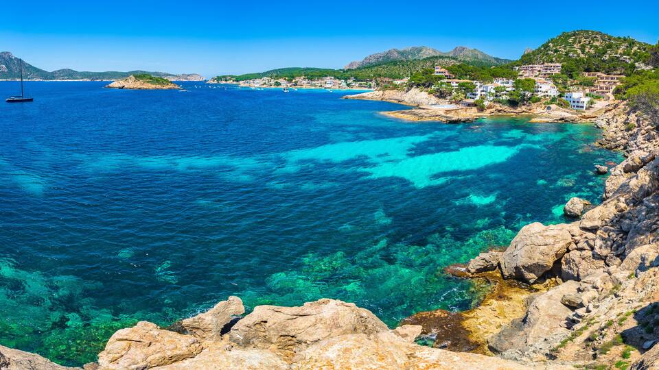 A coastal landscape with clear blue waters, rocky cliffs, and a sailboat.