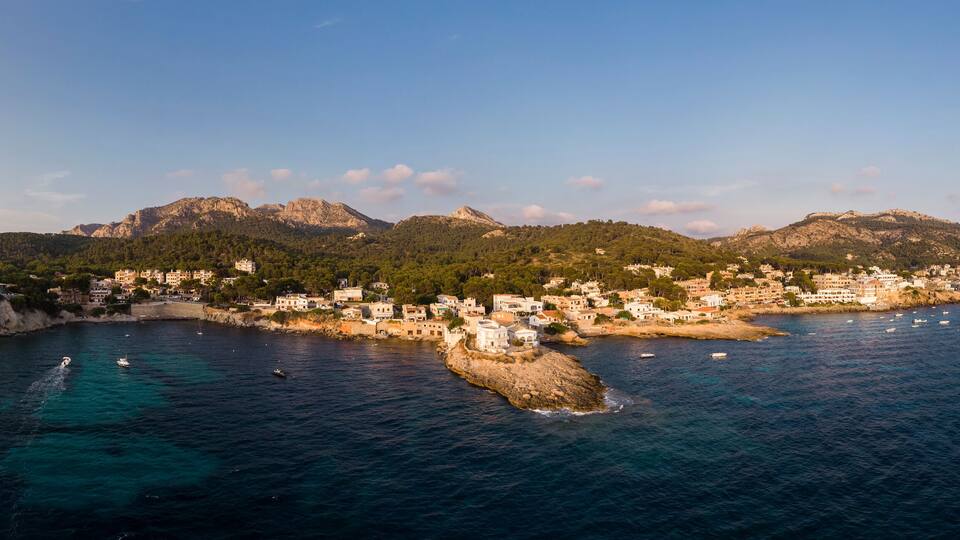 A coastal town with buildings along the shoreline, surrounded by mountains and clear blue waters.