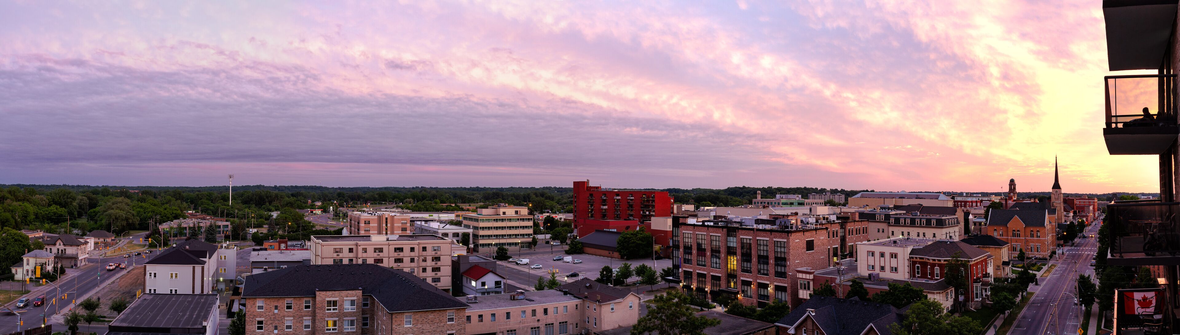 A cityscape at sunset with a prominent red building, a church spire, and a mix of residential and commercial buildings.