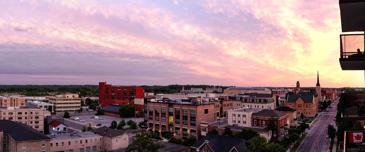 A cityscape at sunset with a prominent red building, a church spire, and a mix of residential and commercial buildings.