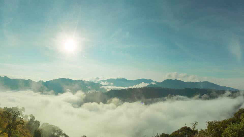 A mountain range with a sun shining through the clouds.