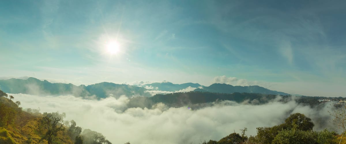 A mountain range with a sun shining through the clouds.