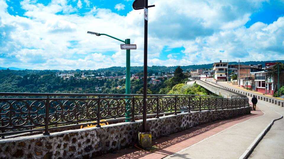 A stone wall with a metal railing, a pedestrian walkway, and a view of a town in the distance.