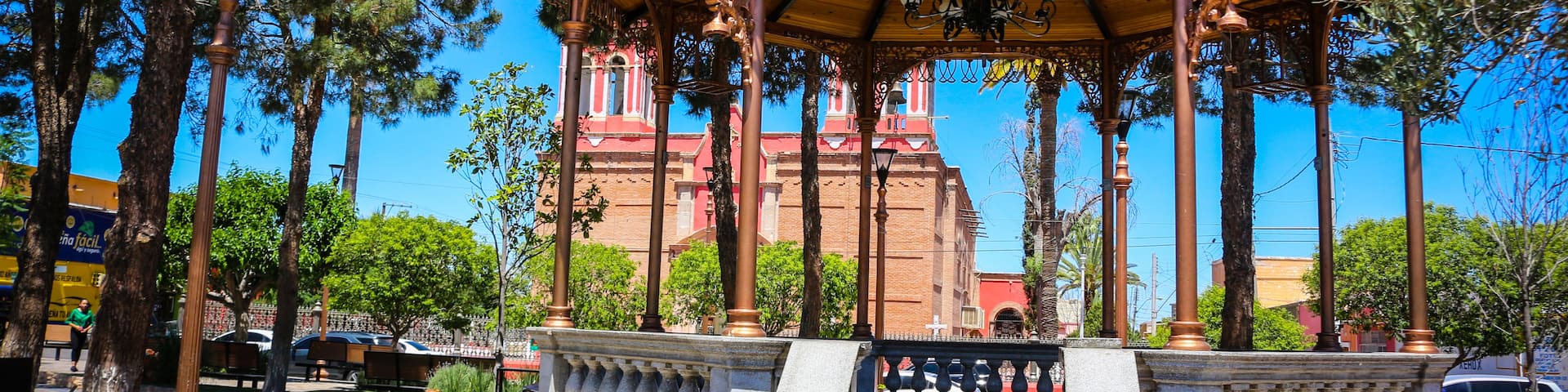 A gazebo with ornate metalwork and a red building in the background.