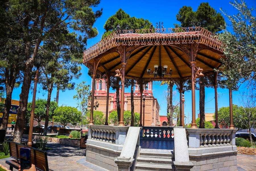 Un mirador con ornamentación metálica detallada y un edificio rojo al fondo.