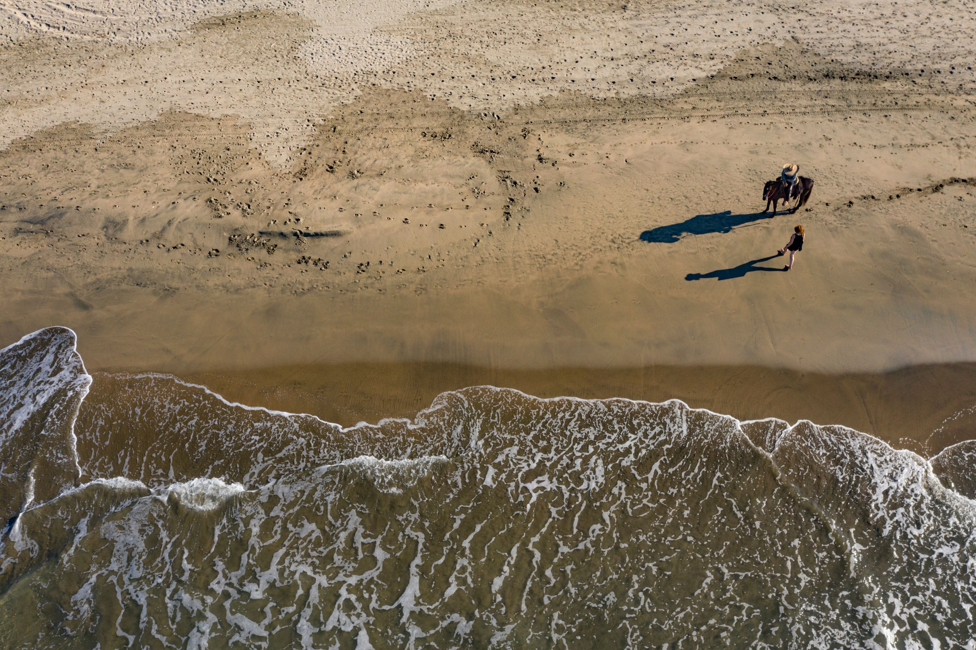 Aerial view of tranquil Playa Troncones beach with a horse casting a shadow on the sandy shoreline, Guerrero, Mexico.