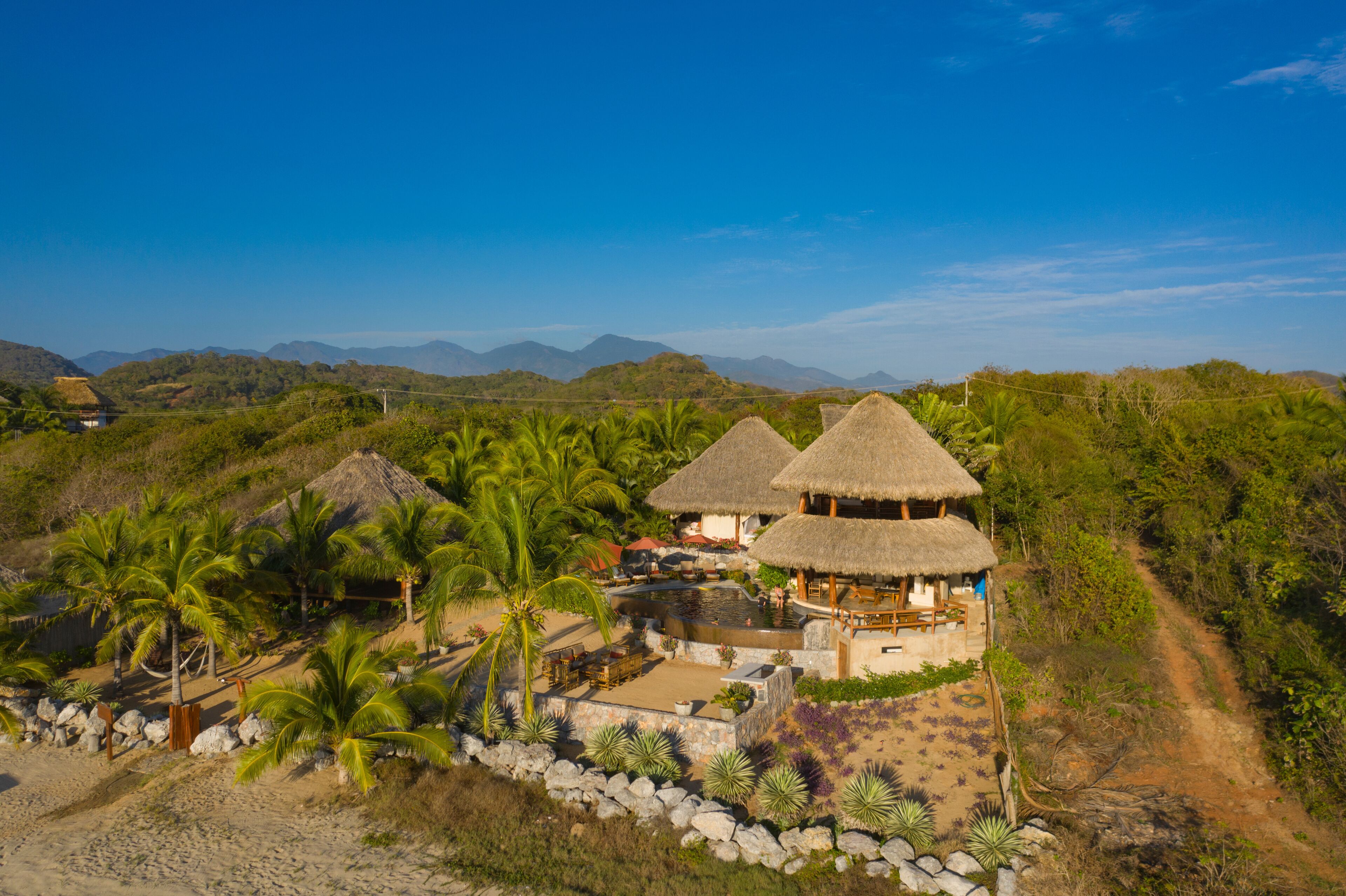 Aerial view of luxury villa with thatched roof surrounded by palm trees and ocean, Troncones, Mexico.