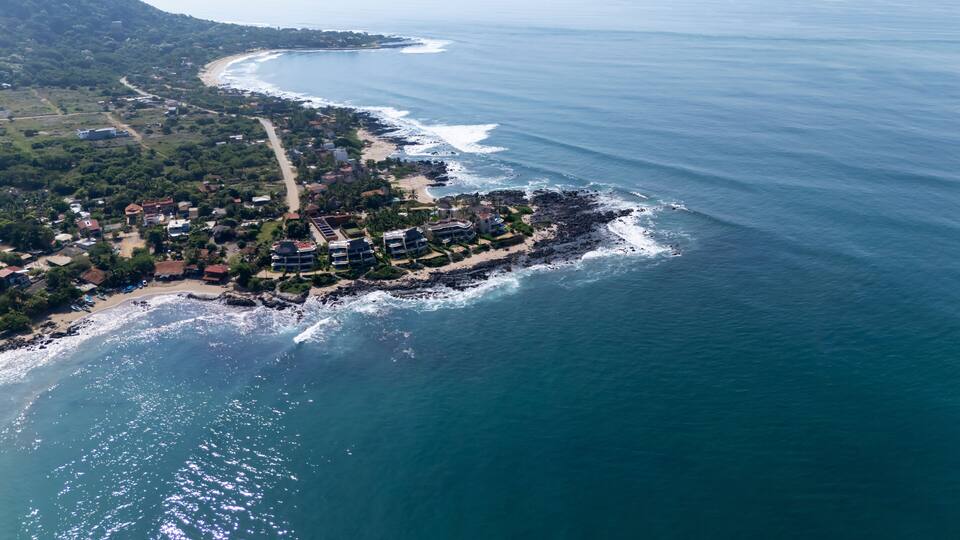 An aerial view of a coastal town with a beach, rocky shoreline, and residential buildings.