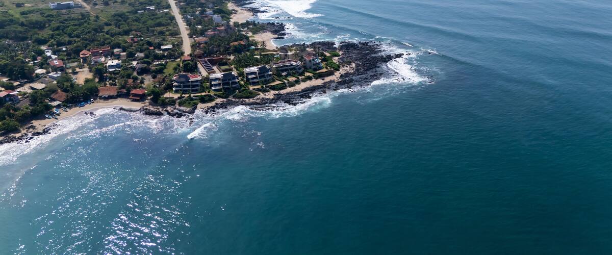 An aerial view of a coastal town with a beach, rocky shoreline, and residential buildings.