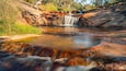 A waterfall cascading over rocks into a pool, surrounded by greenery.