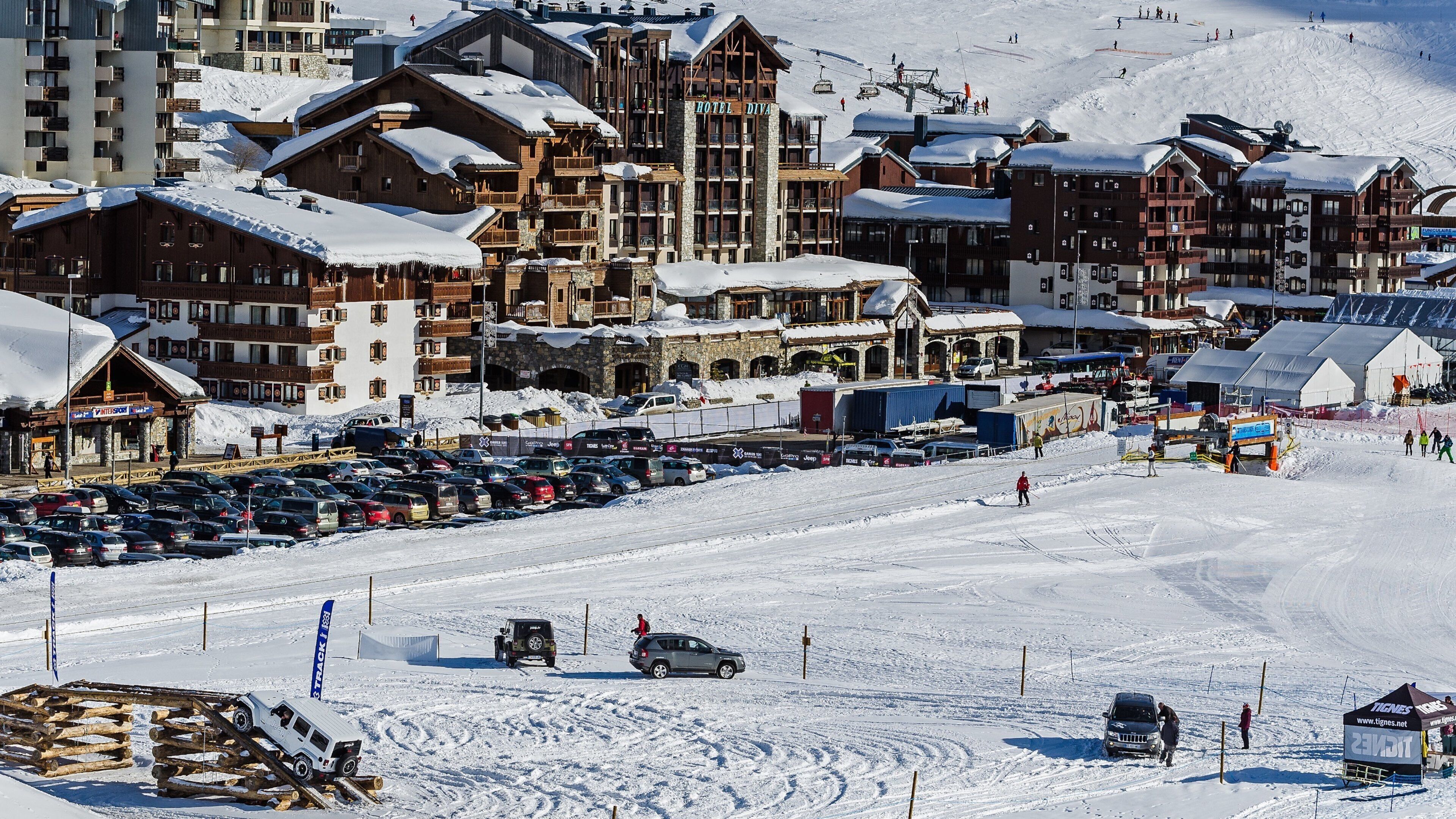 A snow-covered ski resort with a hotel named "Hotel Diiva," a ski lift, and a parking area filled with cars.