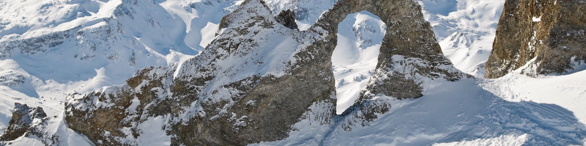 Una montaña nevada con un arco rocoso destacado.