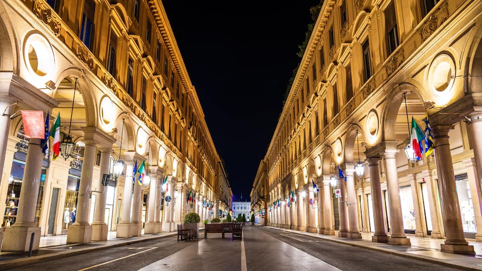 Una vista notturna di una strada imponente illuminata, con architettura classica e numerose bandiere nazionali.
