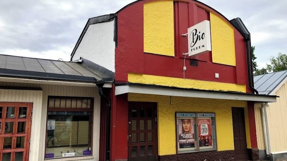 A building with a red and yellow facade, a sign reading "Bio", and a poster advertising a show.