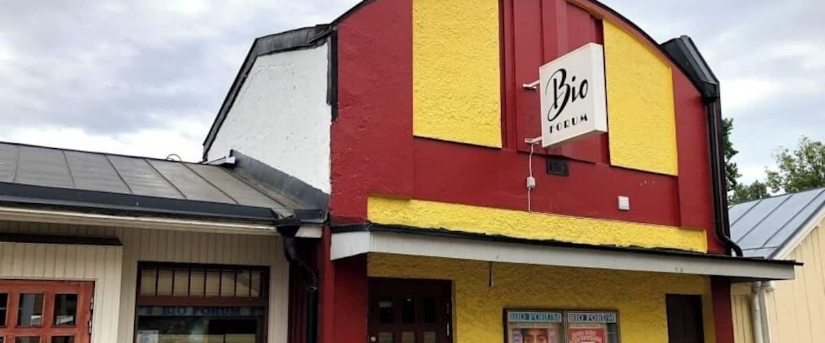 A building with a red and yellow facade, a sign reading "Bio", and a poster advertising a show.